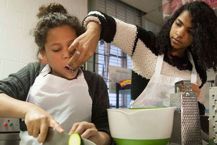 Tatiana Castillo gets a taste of cheese from classmate Brittany Jones while cutting vegetables for a quiche that will be made at Roberto Clemente Middle School.