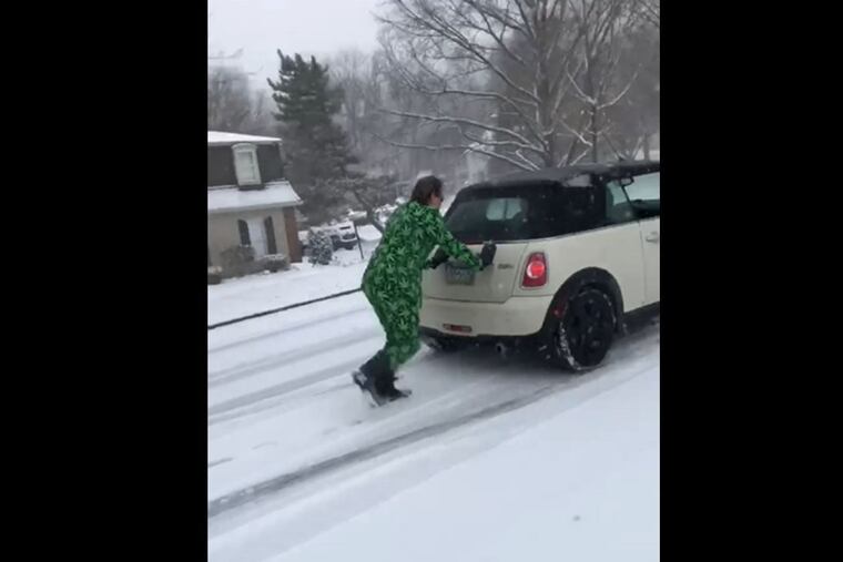 A screenshot of a video of Cary McClain, a Main Line defense attorney, pushing a Mini Cooper up a hill while wearing a weed suit.