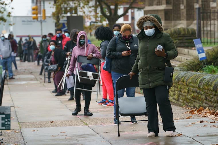 Awa Traore (front) picks up her chair Monday as the line of people waiting to vote moves forward, at Tilden Middle School in Philadelphia. Tuesday is the last day for voters to request mail ballots, including at satellite elections offices around the city.