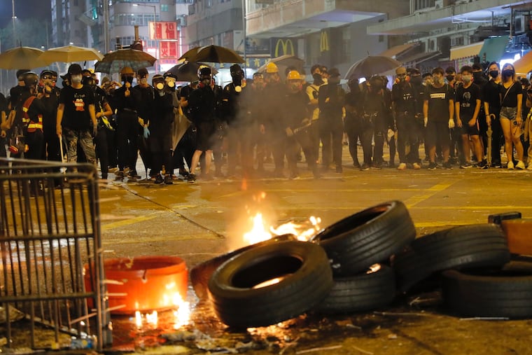 Black-clad protestors stand near burning tires in Hong Kong, Tuesday, Oct. 1, 2019.