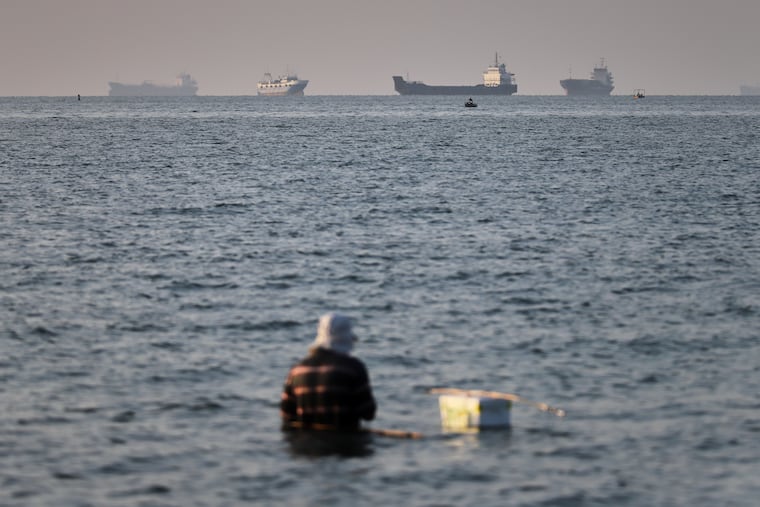 A person sits on shallow water as cargo and commercial vessels are anchored in the Strait of Hormuz off Bandar Abbas, Iran, Monday, June 8, 2026.