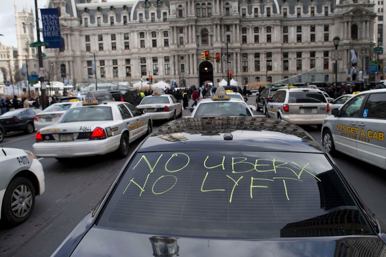 In this February 2016 file photo, taxis and Uber Black cars — one with a message — park in front of City Hall as their drivers demand better regulation of Uber X.