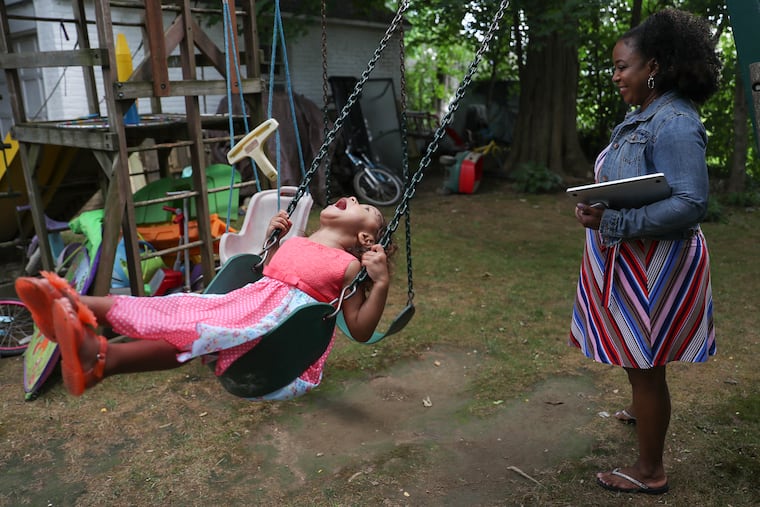 Bethany Watson-Ostrowski holds her laptop and work phone before a Zoom call with her boss while her youngest daughter, Julie Ostrowski, 3, plays on the swings outside of their Cheltenham home.