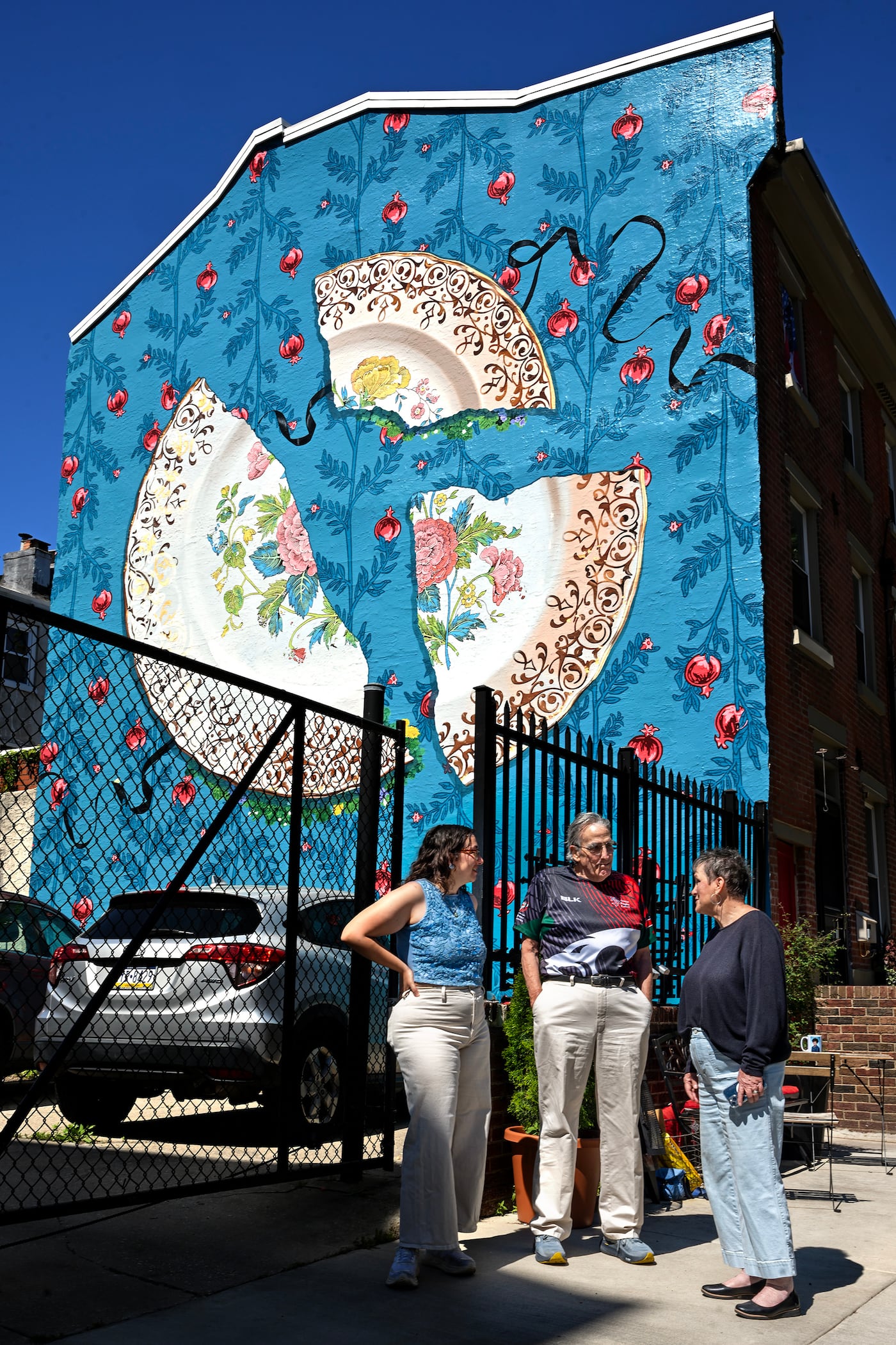 Artist Sammy Kovnat (left) talks with homeowners Sara and Clark DeLeon in front of their mural.