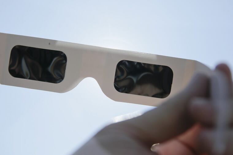 High-quality solar eclipse viewing glasses block out nearly 100 percent of the sun’s rays, says Wills Eye Hospital attending surgeon Jack Dugan, holding a pair up to the sun outside his office in Voorhees.