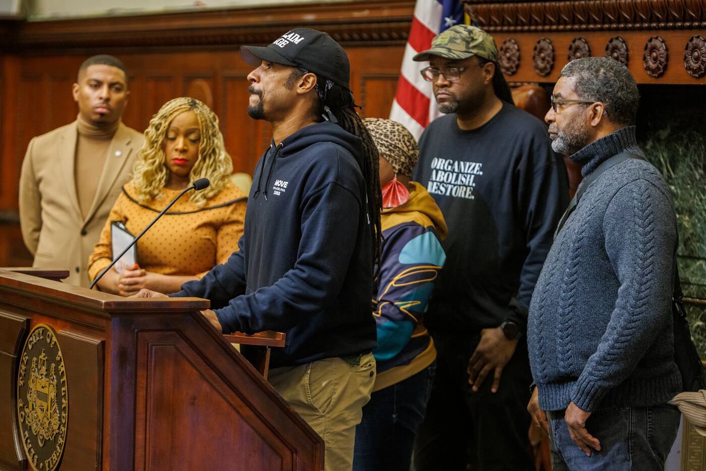 Mike Africa Jr. speaks at a news conference on Dec. 9, 2024, calling for the Penn Museum to return the remains of Delisha Africa. In the background from left are Councilmembers Nicolas O’Rourke and Jamie Gauthier, Yvonne Orr-Ell, Gabe Bryant, and Basym Hasan.