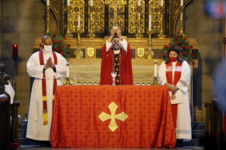 Rev. Darrell Tiller (izquierda) y la reverenda Yesenia "Jessie" Alejandro (derecha) están de pie mientras el obispo Daniel Gutiérrez rompe una hostia para la comunión, durante su ceremonia de ordenación en la Iglesia Episcopal St. John en Norristown, Pensilvania, el sábado 10 de octubre de 2020.