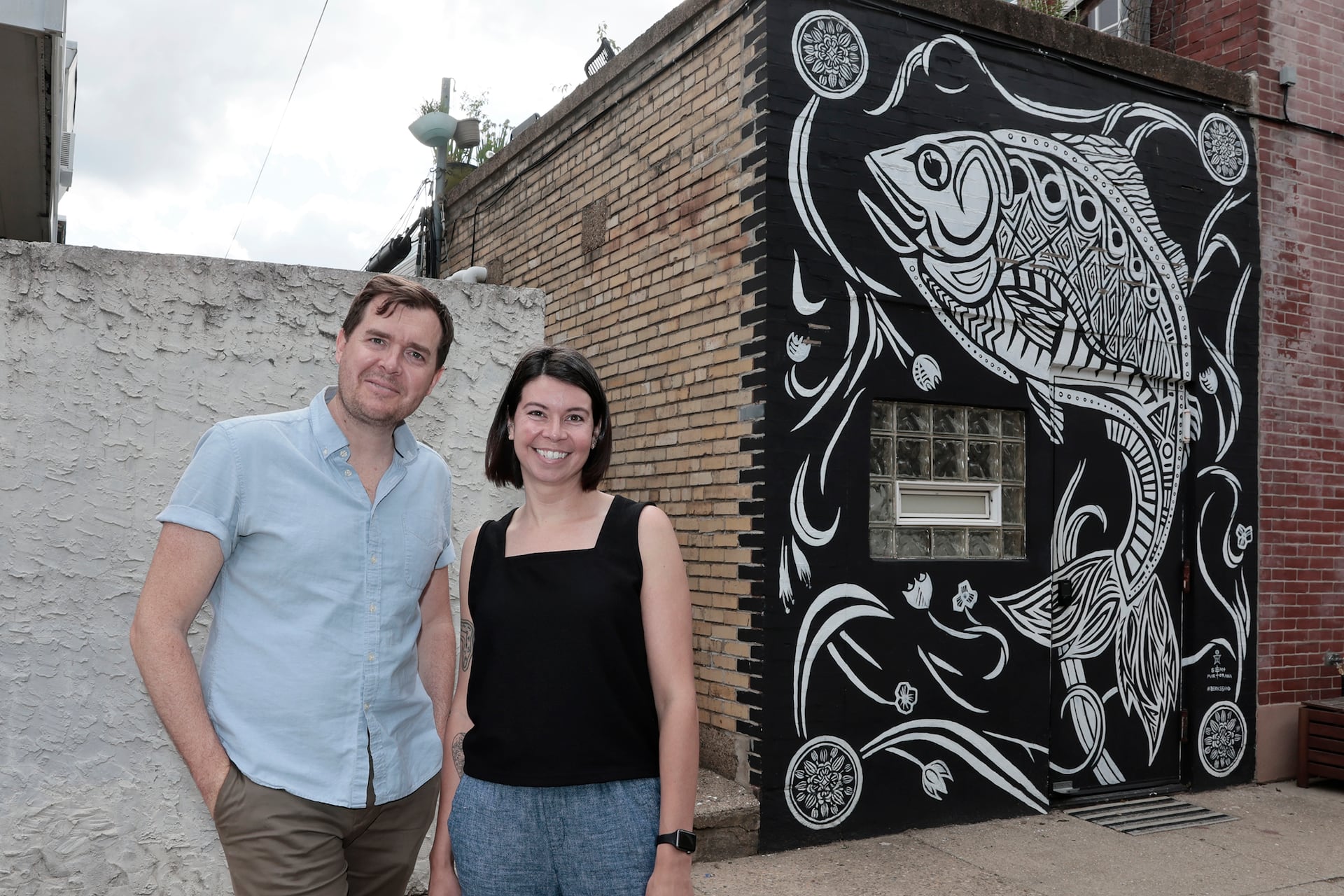 Christopher and Shannon Wink stand in front of the "Berks Shad" mural on their Fishtown home.
