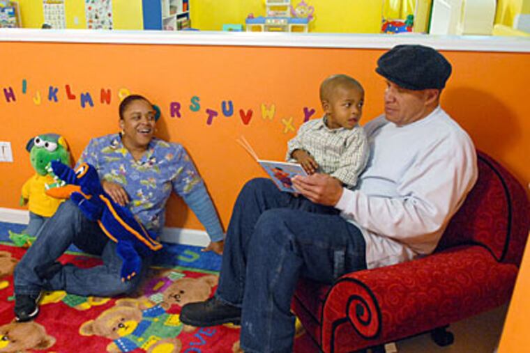 Percy "Buster" Custus holds his grandson, Jasin Custus, 2, inside the newly opened Custus Childcare Academy in West Philadelphia. At left is Shennon Williams, a teacher at the day care. ( Peter Tobia / Staff Photographer )