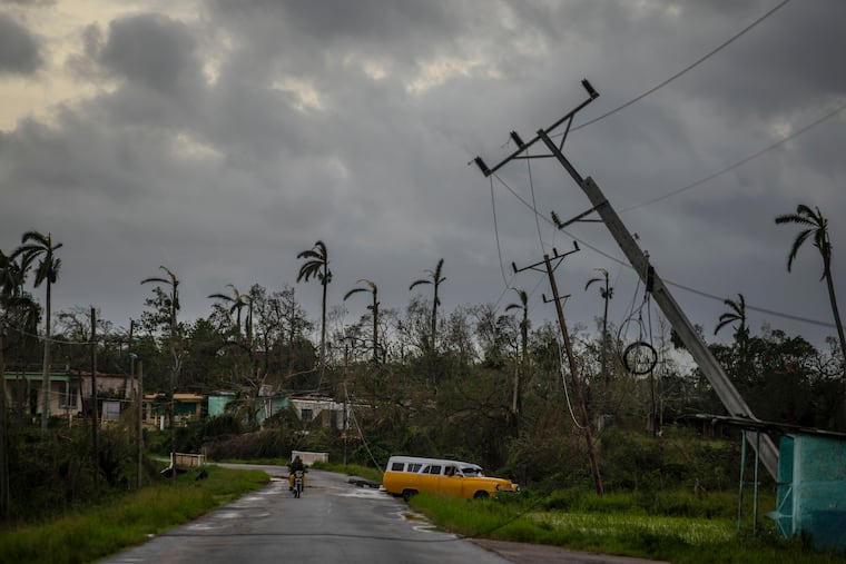 A classic American car drives past utility poles tilted by Hurricane Ian in Pinar del Rio, Cuba, Tuesday, Sept. 27, 2022.