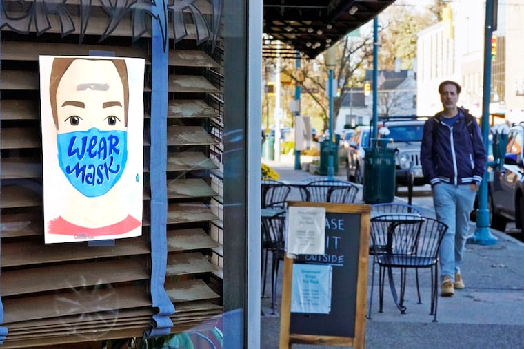 A man walks past a restaurant in Mount Lebanon, Pa., with a sign in the window that reminds people to wear a mask, Wednesday, Nov. 18, 2020. Recent measures shuttered indoor dining in the state until Jan. 1.