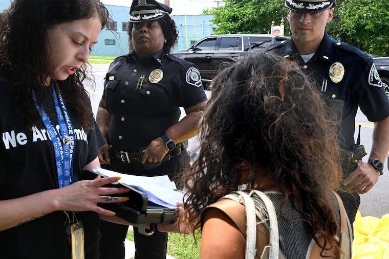 Center for Family Services lead counselor Lyzza Tyson (left) works with Camden County Metro Police Capt. Vivian Coley (center) and Lt. Luis Gonzalez (right) talking with an unhoused person living in the park at Waterfront South Raingardens Wednesday, July 16, 2025. Some of the department’s new social workers are stationed inside the downtown police headquarters for walk-ins while others are deployed in the field alongside officers doing door knocks, engaging transients at encampments, and making referrals for social services.