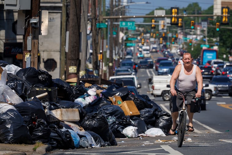 Cyclist riding beside large garbage dump along Allegheny Avenue at C Street in Philadelphia. AFSCME District Council 33 workers enter their second week on strike, Tuesday, July 8, 2025.