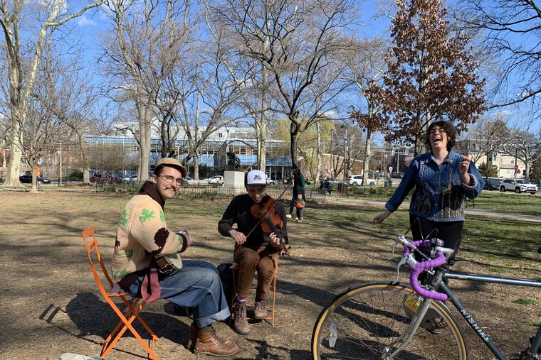 Ovi Horta on banjo and Jordan Rast on fiddle play as a passerby dances in Clark Park in Philadelphia on Sunday.
