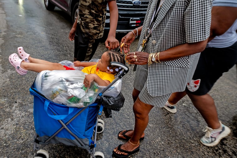 Caroline Small wheels her 2-year-old great-granddaughter atop a bag of trash as she carts it to a drop-off site at the Tustin Playground at 60th Street and West Columbia Avenue. Residential trash collection stopped when a strike was called by District Council 33. Small lives just around the corner and said of the toddler, “She was just walking too slow.” Scene Through the Lens runs every Monday on page B-2. There is a template in Roxen. This sentence runs at the top of the photo: More of photographer Tom Gralish’s visual exploration of our region can be seen in his blog at Inquirer.com/sceneontheroad.
