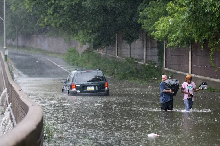 Bob Dugon (left) helps his friend Kiearra Price retrieve belongings from her car after it was caught in floodwaters on West Hunting Park Avenue at Ridge Avenue last month as Fay doused the region with heavy rains.
