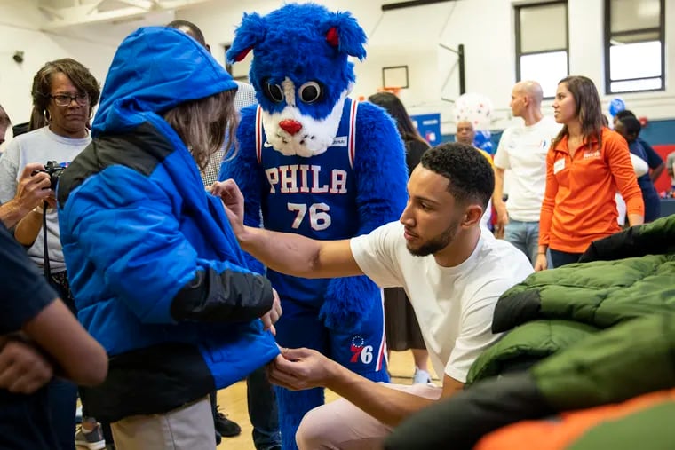 76ers guard Ben Simmons helps zip the winter coat on a student from Henry C. Lea Elementary School.