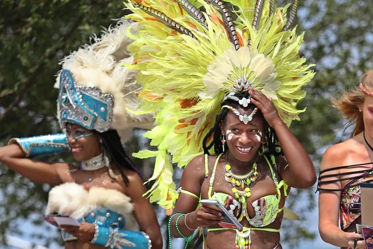 Kristina Hill,right, representing Jamaica, holds onto her headdress as the wind tries to take it off her head as she and Khenti Pratt, left, representing the Bahamas, walk through the 30th Annual Philadelphia Caribbean Festival in 2016. 
