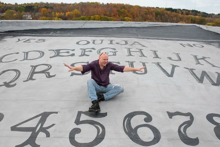 Blair Murphy poses with the world's biggest Ouija board he created on the roof of the 'haunted' Grand Midway Hotel in Windber, Pa., Somerset County.