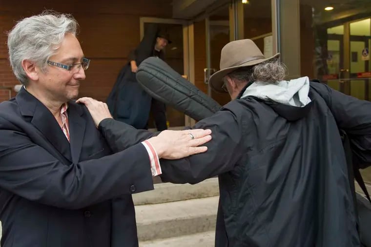 Philadelphia Orchestra cellist John Koen, chairman of the players' negotiating team, is greeted by bass player John Hood (right) bringing his instrument back into the Kimmel Center Sunday, after the musicians voted to ratify a new contract.