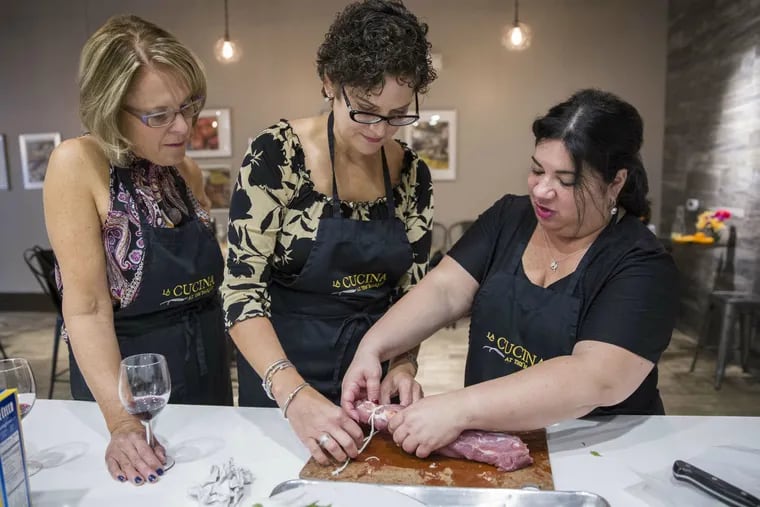 At La Cucina at the Market, instructor Agnes DeMarco (right) shows Holly Nase (left) and Dale Cardarelli how to tie twine around a stuffed pork tenderloin.