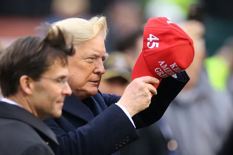 President Donald Trump puts on a hat that says "KEEP AMERICA GREAT" before the 120th Army-Navy game at Lincoln Financial Field in South Philadelphia on Saturday, Dec. 14, 2019.