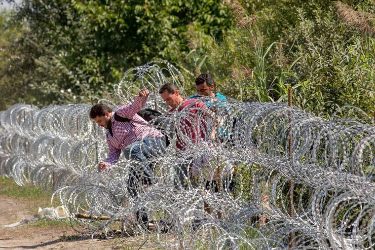 Migrants jump over razor wire strung along the border, where Hungarian soldiers have already laid low-level fortifications.