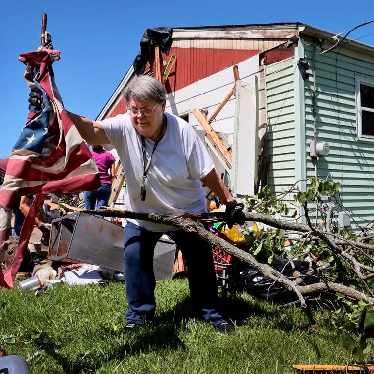 Patti Manley, 69, moves a shredded American flag as she gathers branches from the backyard of her mother's home on Morningdale Place in Mehlville, Mo., on Monday, May 27, 2024, following a violent storm and possible tornado Sunday evening. Manley was staying with her mother Jackie Moloney, 88, when the storm hit. She and her mother rode it out in an interior bathroom.