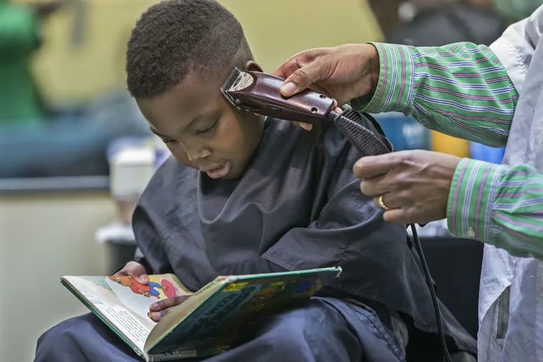 Jordan Brown, 8, reads a book while getting a haircut at D & D's barbershop in Woodbury. The Evergreen Avenue Elementary third grader is in a program that offers discounts to students who read while getting their hair cut.