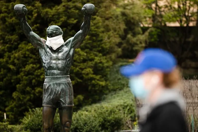 FILE - In this April 14, 2020, file photo, a person wearing a protective face mask as a precaution against the coronavirus walks past the Rocky statue outfitted with mock surgical face mask at the Philadelphia Art Museum in Philadelphia. (AP Photo/Matt Rourke, File)