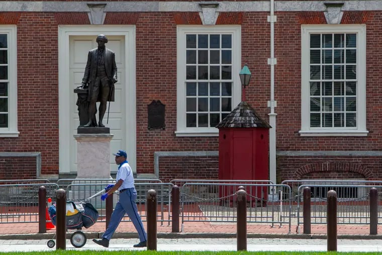 A U.S. Postal Service carrier walks past a statue of President George Washington in front of Independence Hall in Old City, Philadelphia on Friday, Aug. 7, 2020.