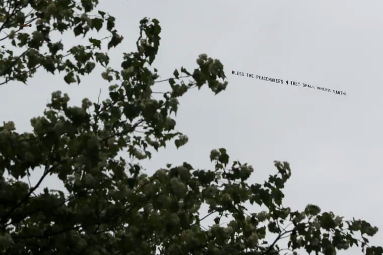 A prop plane flies over Center City towing a banner that reads "Bless the peacekeepers 4 they shall inherit [the] earth!"