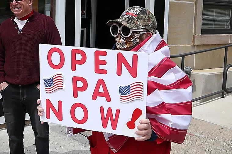 A protester walks by a restaurant open for take-out business as fellow protesters gather outside the Capital Complex in Harrisburg on April 20. They are calling for Gov. Wolf to reopen up the state's economy during the coronavirus outbreak.