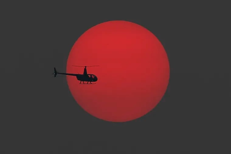 A helicopter flies in front of the red setting sun on Tuesday.  Smoke and particles for the west coast wildfires moved over the Northeast, causing the red sun.