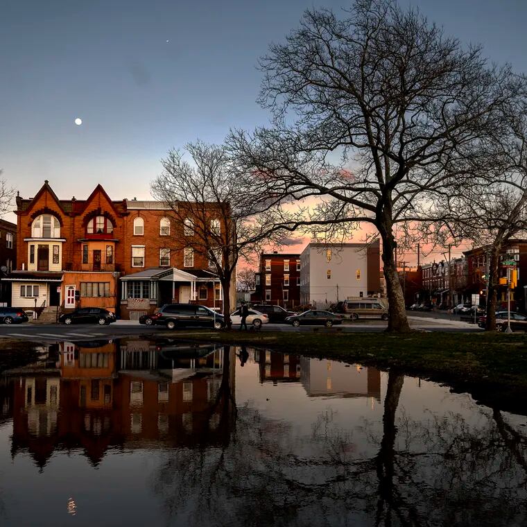 March 20, 2023: The moon rises behind the buildings along North 33rd and Oxford Streets in Strawberry Mansion as the sun sets in front of them following a day of rain.