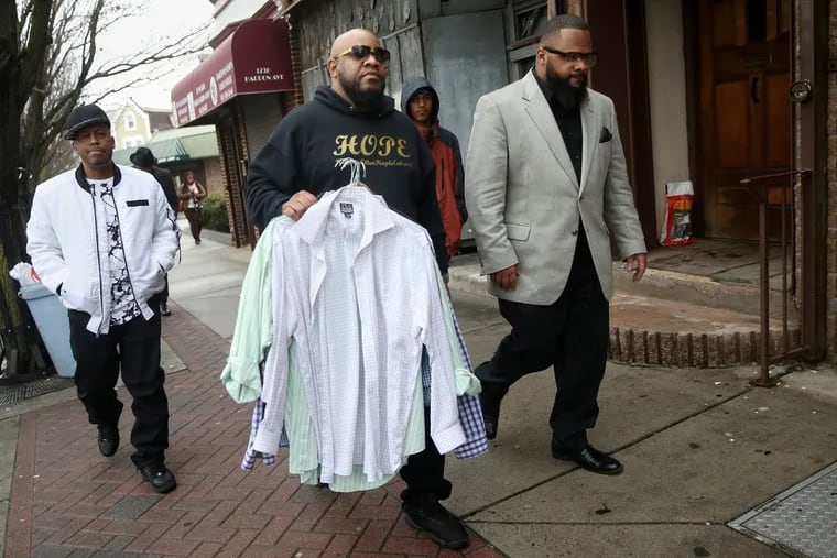 Andre Spruel, center, founder of Helping Other People Eat, a local organization that offers free meals to those in need, walks with Kevin Livingston, right, founder of 100 Suits for 100 Men, as they give away free suits and ties to men in Camden on Saturday, Feb. 24, 2018. TIM TAI / Staff Photographer