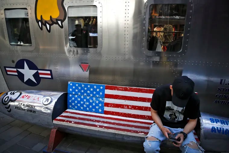 A man in Beijing sits on a bench decorated with a U.S. flag outside a fashion boutique selling U.S. brand clothing.