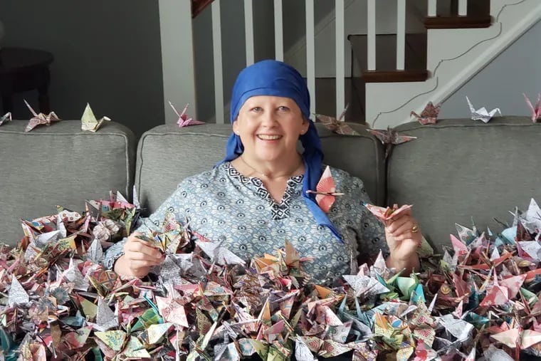 Beth Carlough, enveloped in the 1,000 origami cranes her friend Wendy Nowicki made to send her a message of love, support, and wishes for good health while Beth was undergoing cancer treatment.  Between the pandemic and Beth's supressed immunity, Wendy could not hug her, but she could touch every one of these cranes.