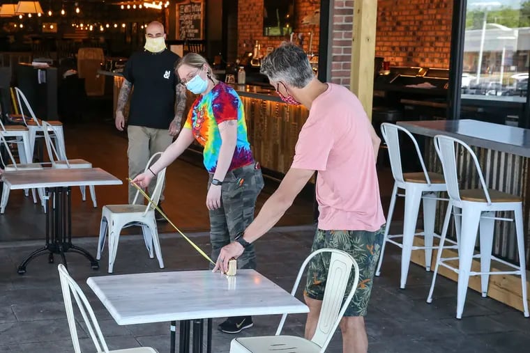 At the Stove & Tap in Malvern owner Justin Weathers holds the tape measure as Caitlin Welge goes for a six foot distance between tables, Tuesday, May 26, 2020. Fewer Pennsylvanians are filing new claims for unemployment benefits as businesses start to reopen.