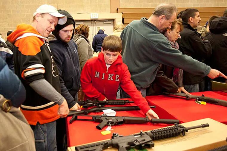 Mike Stout and his sons Ryan, 23, and Michael, 11, look over semi-automatic rifles at the Philadelphia National Guard Armory Gun Show in Jan. 2013. The Stouts live in Philadelphia. ( ED HILLE / Staff Photographer )