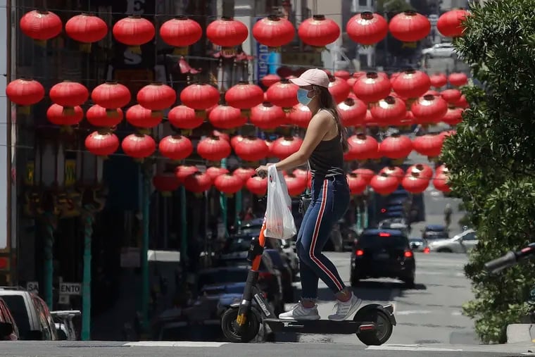In this July 11 photo, a woman wears a face mask while riding a scooter in front of lanterns hanging in Chinatown in San Francisco.