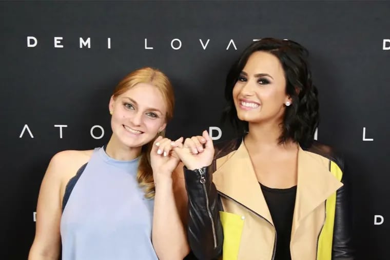 Hannah Cooper and Demi Lovato lock pinkies at concert.