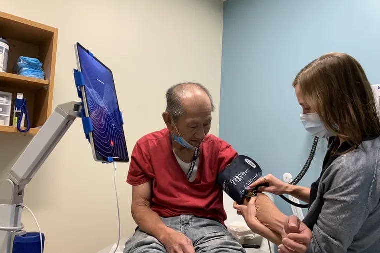 Jessica Deffler, a doctor at the Wyss Health Center, checks Tong Trinh's blood pressure during an examination. An interpretation app through a tablet next to them helps the Vietnamese immigrant and doctor communicate.
