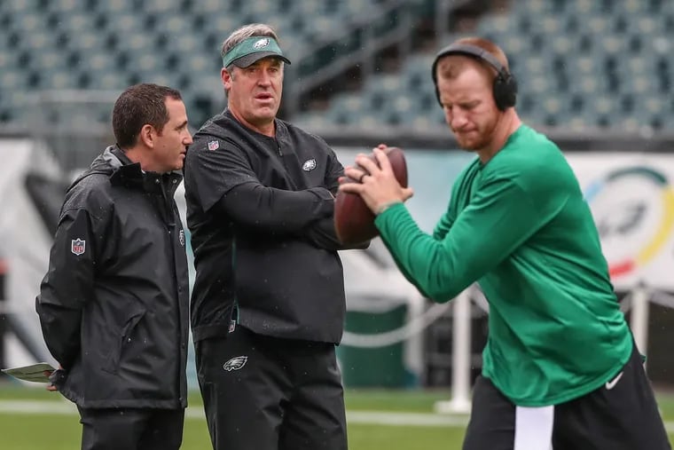 Eagles coach Doug Pederson (center) watches quarterback Carson Wentz (right) warm up while talking to general manager Howie Roseman in 2018.