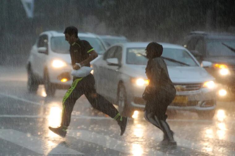 Pedestrians caught in a downpour race across the intersection of JFK Boulevard and 15th Street in Center City. About 6 p.m. Sunday, the skies darkened and a deluge opened up on Philadelphia, but within about 15 minutes sunlight was visible again.