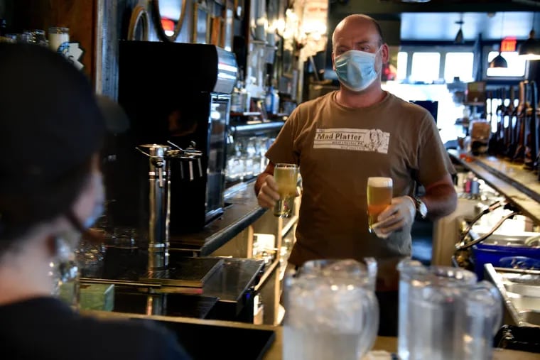 Working behind the bar at Second District in South Philadelphia, bartender Paul Dellevigne brings beer to server Danielle Dubois to take to outside diners.