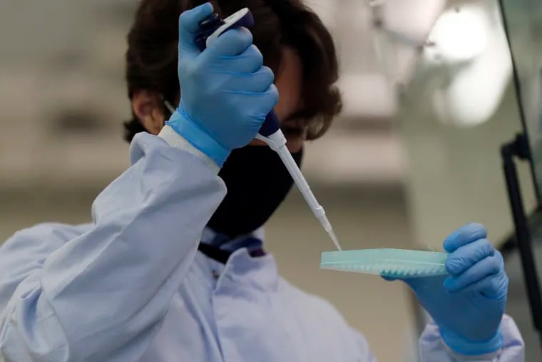 A lab assistant uses a pipette to prepare coronavirus RNA for sequencing at the Wellcome Sanger Institute that is operated by Genome Research in Cambridge, Mass.