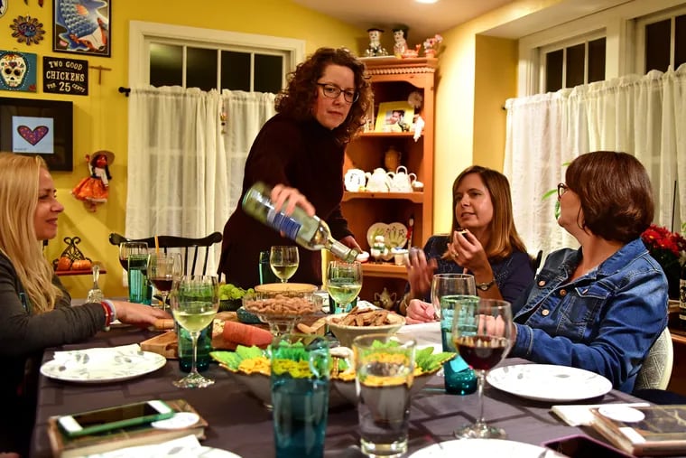 Alison Goldberg (standing) pours wine as she hosts book club at her Voorhees home October 30, 2018. At left is Charmaine Young. Janine Shinkle (left) and Lisa Earle (right) are on the right. They are using Book Club in a Bag.