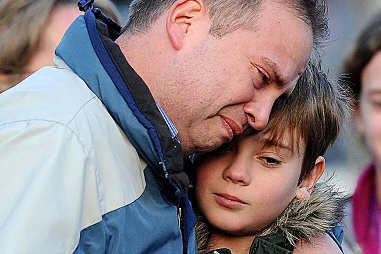 A day after the massacre at Sandy Hook Elementary School, a man holds a child close as they visit a memorial in Newtown, Conn., that mourners created nearby. OLIVIER DOULIERY / Abaca Press, MCT