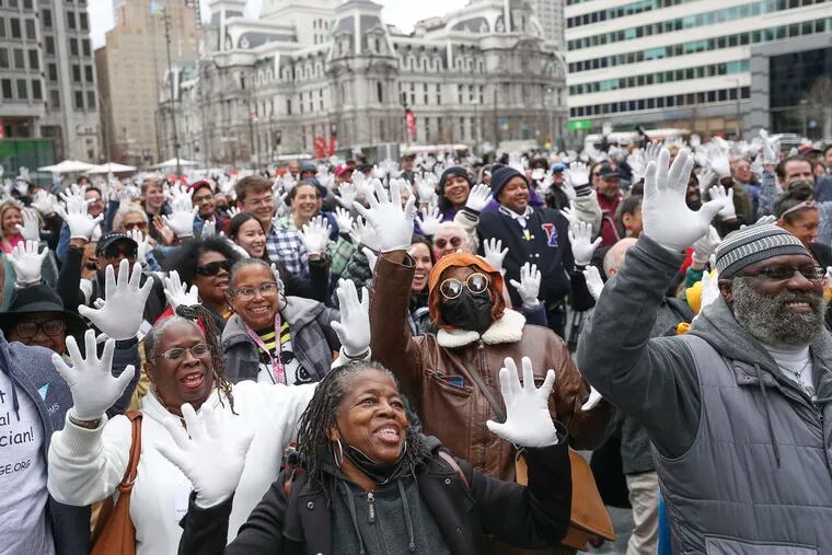People put up their jazz hands with free white jazz gloves they received at the Philly Celebrates Jazz 2023 Kickoff Event in Love Park.